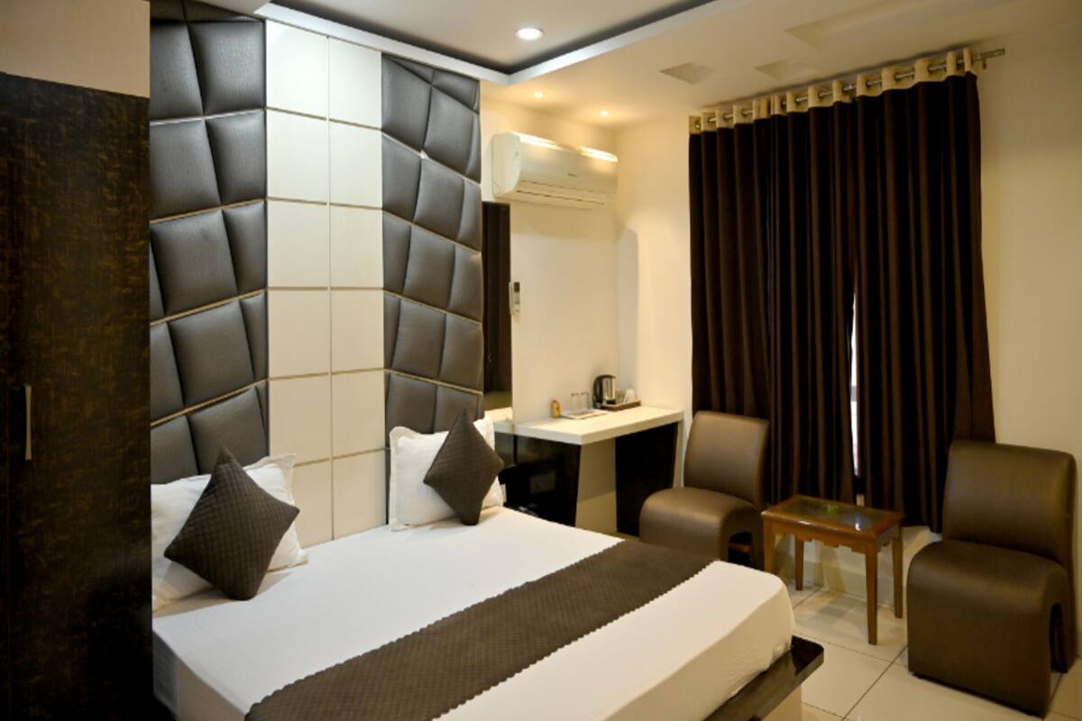 A modern hotel room with a large bed, a desk, a chair, and a small table.