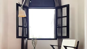 A room with a large window, a chair, a small table with a vase, and a lamp. - 5H Garden  (Ho Chi Minh City)