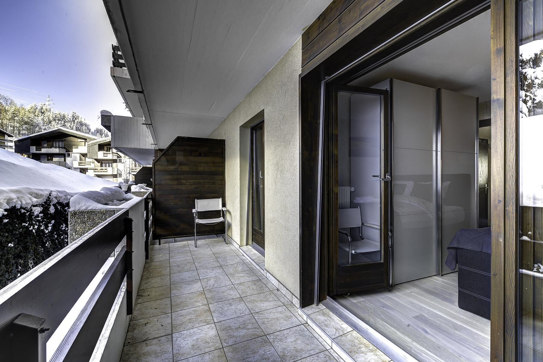 Ein modernes Hotelzimmer mit Balkon, einer Schiebeglastür und Blick auf die verschneite Landschaft.