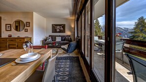 Una sala moderna con una mesa de comedor de madera, un sofá y un amplio ventanal con vistas a la montaña.
