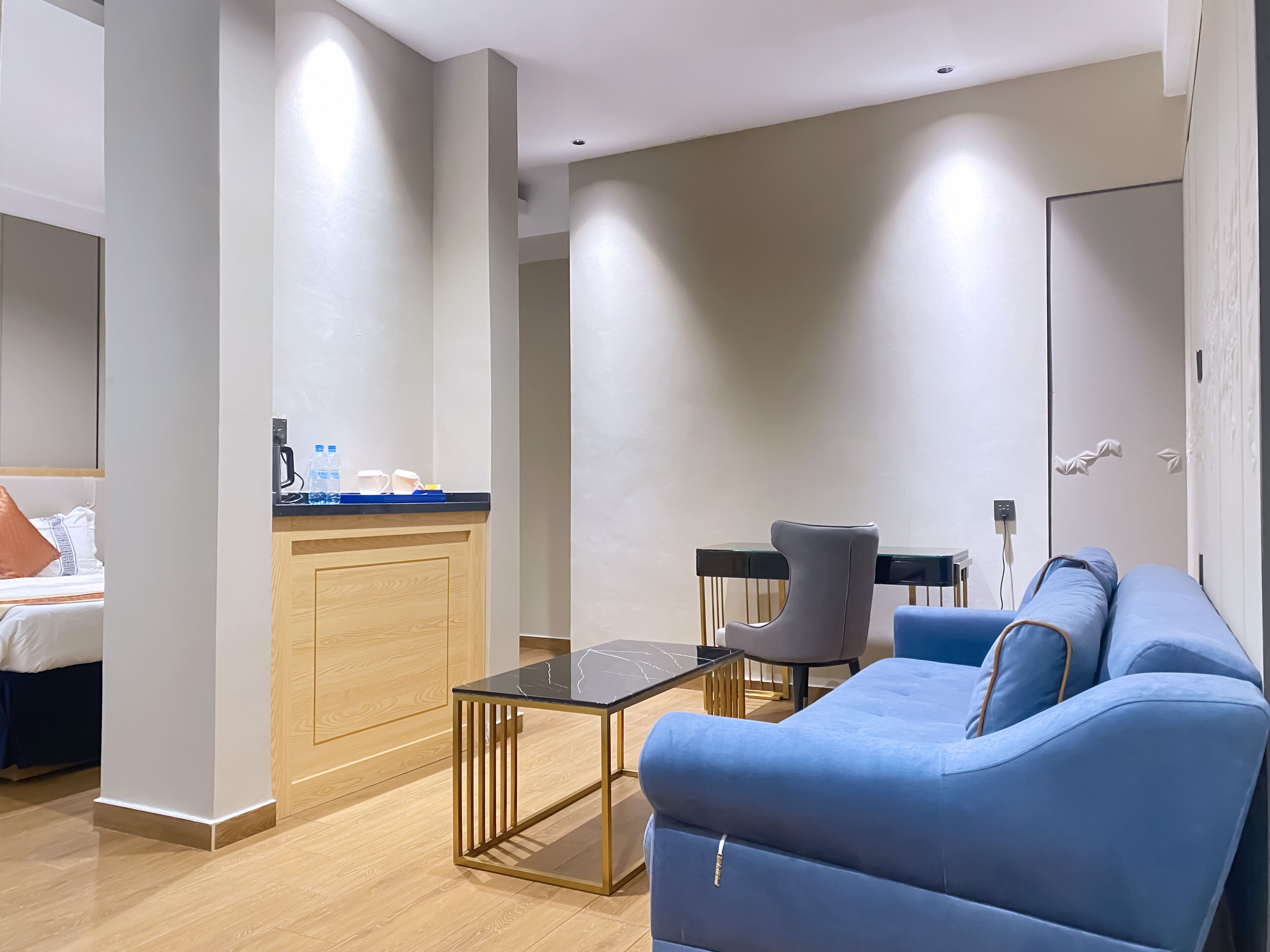 A modern hotel room with a blue sofa, a small table, and a kitchenette area.