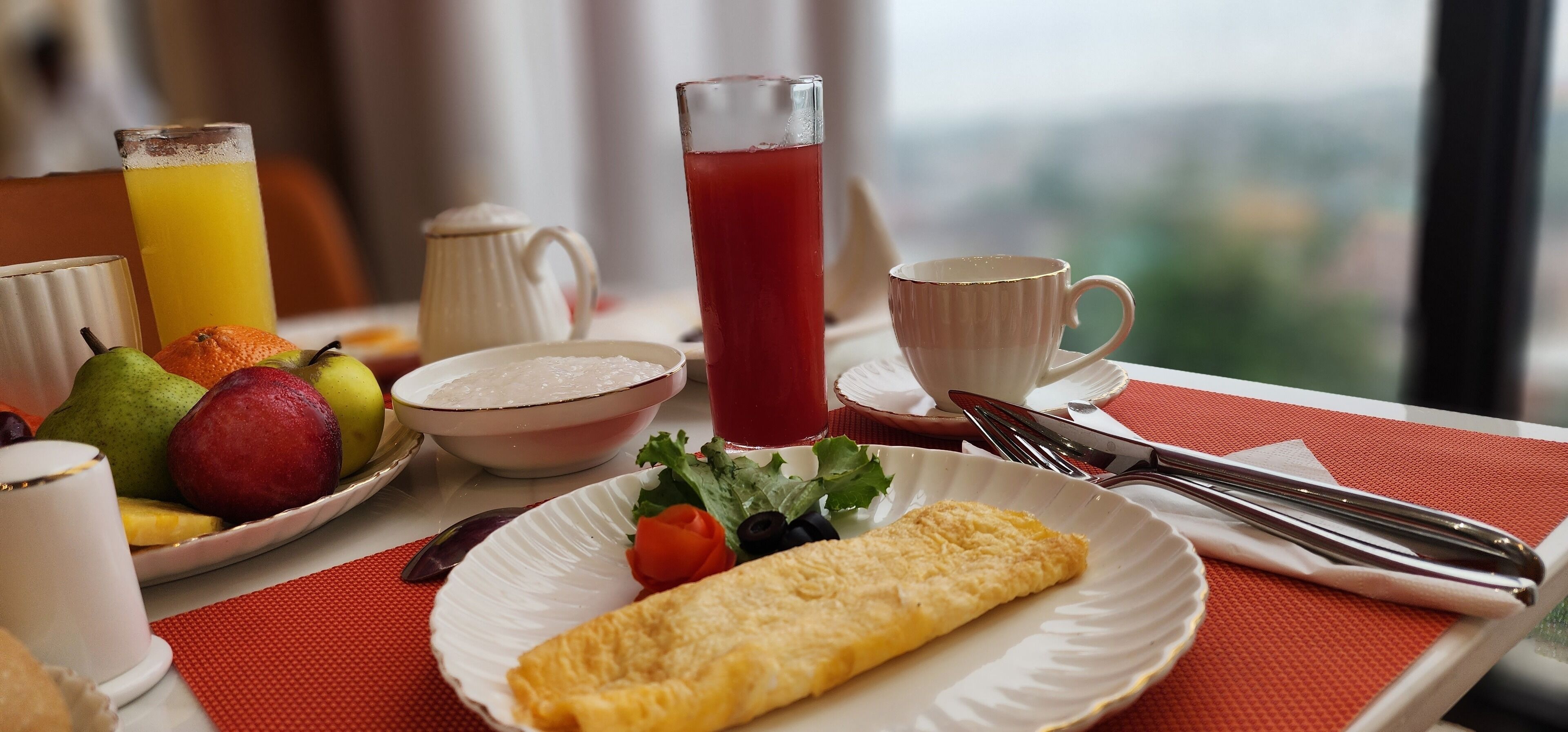 A breakfast tray with an omelette, fruit, a pitcher of red juice, a cup of coffee, and a teapot.