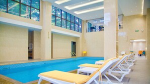 A swimming pool with sun loungers and a view of the outdoors through large windows. - FM HOTELS (Abidjan)