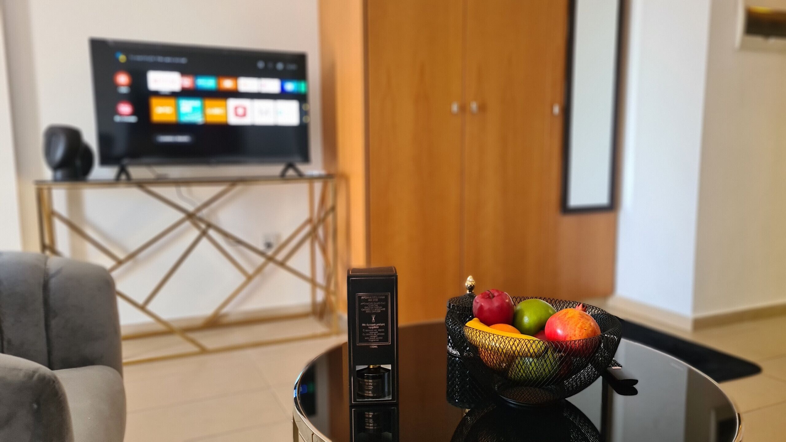 A living room with a TV on a stand, a coffee table with a fruit bowl, and a door in the background.