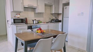 A compact kitchen with a microwave, stove, and refrigerator. There is a dining table with chairs and a bowl of fruit.
