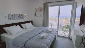 A hotel room with a bed, a view of the city through large windows, a clock on the wall, and a flat-screen TV mounted on the wall. - STAY Napa Living 41 (Ayia Napa)