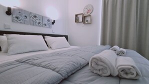 A neatly made bed with a grey quilt and rolled towels, white pillows, and a headboard. - STAY Napa Living 39 (Ayia Napa)