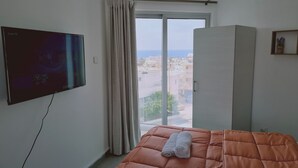 A hotel room with a bed, a TV, a wardrobe, and a window with a city view.