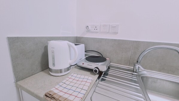 A kitchenette with a coffee maker, toaster, and electric kettle on a countertop, a towel, and a sink with a faucet.