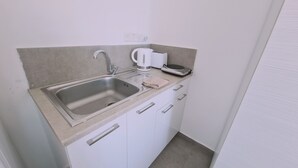 Una pequeña kitchenette con un lavamanos de acero inoxidable, una tetera, un tostador y una balanza.