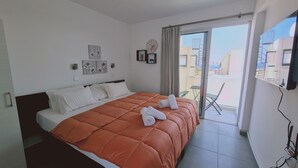Habitación de hotel con una cama grande, un balcón con vistas a edificios y un reloj en la pared.