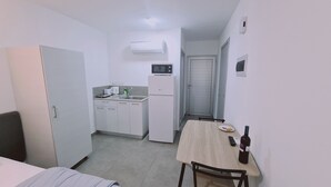 A compact hotel room with a kitchenette, a bed, a small dining table, and a bottle of wine.