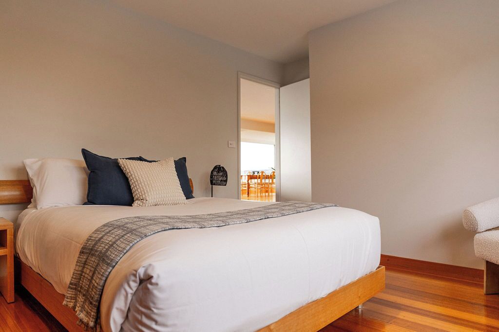 Een keurig opgemaakt bed met houten frame, een nachtkastje en een stoel.