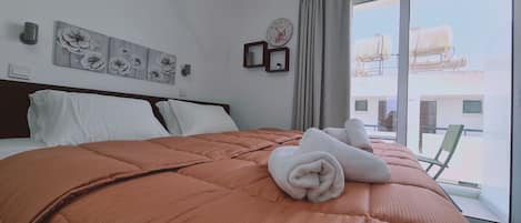 A hotel room with a large bed, a view of the city through the window, and a clock on the wall.