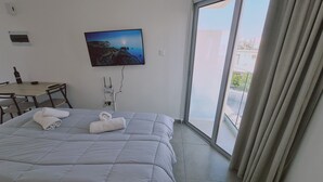 Hotellihuone, jossa on sänky, työpöytä, seinälle asennettu televisio ja liukuovesta avautuva näkymä ulos.