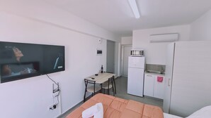 Une chambre d’hôtel compacte dotée d’une télévision à écran plat, d’une petite table à manger, d’une kitchenette équipée d’un four à micro-ondes et d’un lit avec une tête de lit orange.