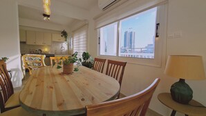 A dining area with a round wooden table, chairs, a lamp, and potted plants. - STAY Naturaleza Penthouse (Limassol)