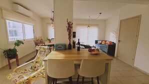A dining area with a wooden table, two chairs, a sofa, and a TV in the background. - STAY Naturaleza Penthouse (Limassol)