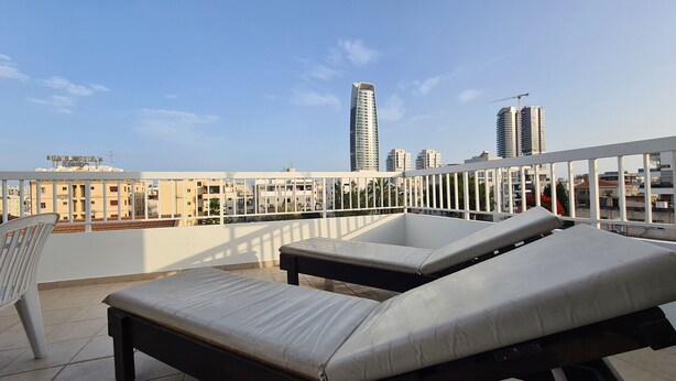 A rooftop terrace with two lounge chairs and a view of city buildings. - STAY Naturaleza Penthouse (Limassol)