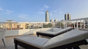 Une terrasse sur le toit, avec deux chaises longues et une vue sur les bâtiments de la ville.