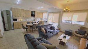 Eine moderne Wohnung mit Wohnbereich, ausgestattet mit einer Couch und Sesseln, einem Esstisch und einer Küche mit Holzschränken und einem Kühlschrank.