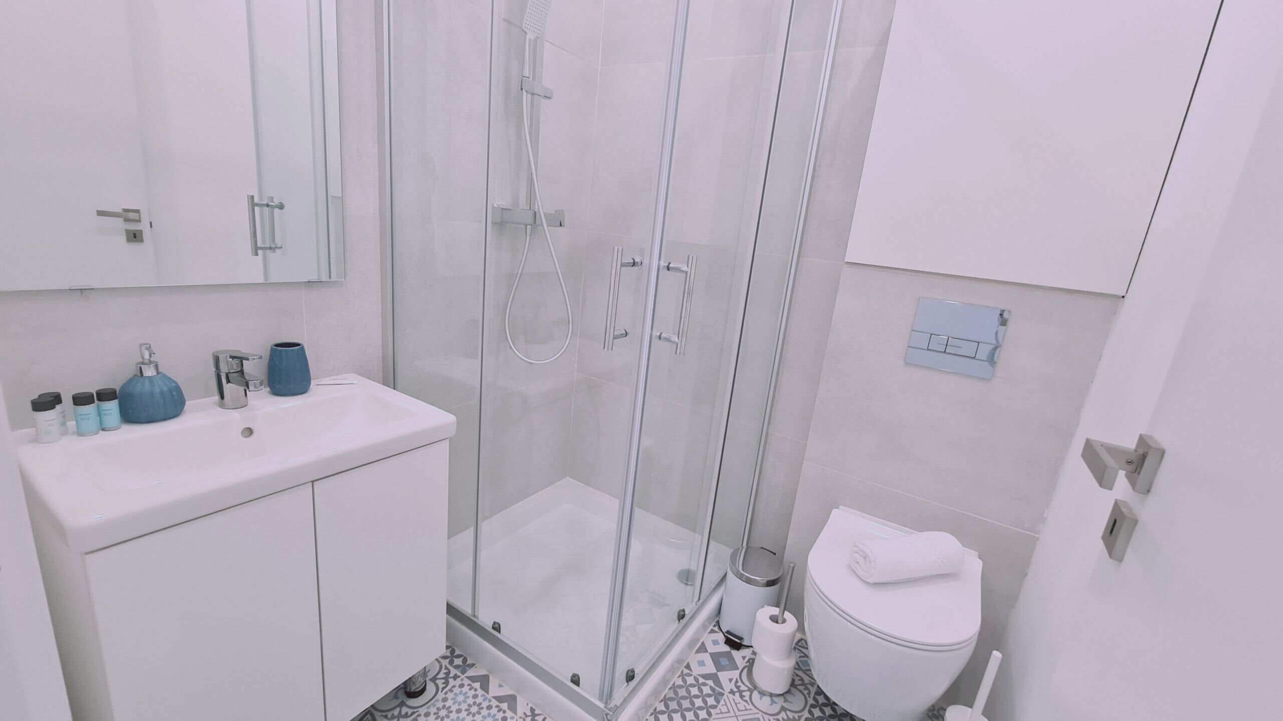 A modern bathroom with a glass-enclosed shower, a white sink with toiletries, and a toilet.