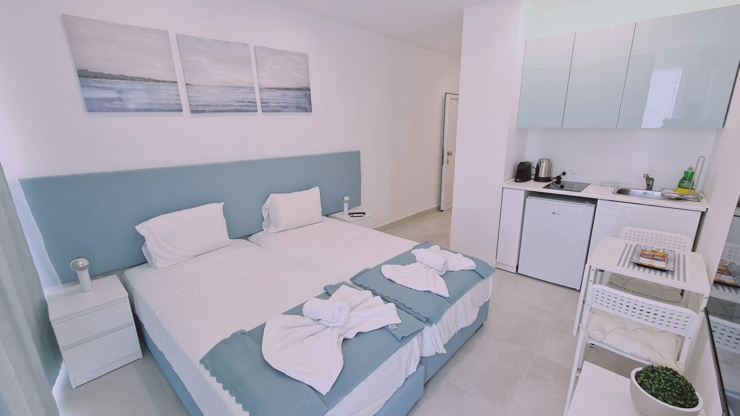 A hotel room with a bed, a nightstand, a small desk, a kitchenette, and a bathroom.