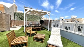 A rooftop patio with wooden furniture, a white cushioned lounge, and a pergola structure. - STAY Napa Aura Apartment (Ayia Napa)