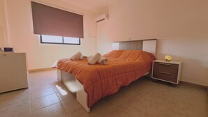 Une chambre à coucher comprenant un lit, une table de chevet, un bureau et une fenêtre avec des stores.
