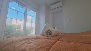 Una habitació d'hotel amb una finestra gran, un aire condicionat i un llit ben fet amb una tovallola arrotllada.