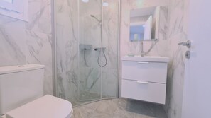 A modern bathroom with a glass-enclosed shower, a toilet, and a vanity with a mirror. - The Getaway (Pyla)