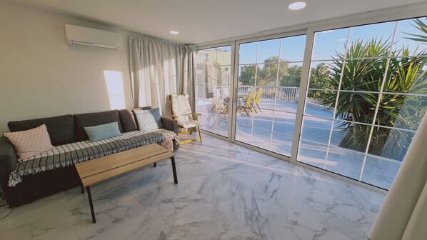 A spacious living room with a large window, a sofa, a chair, and a coffee table. - The Getaway (Pyla)