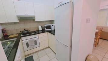 Una cocina compacta con armarios blancos, estufa, microondas y refrigerador.