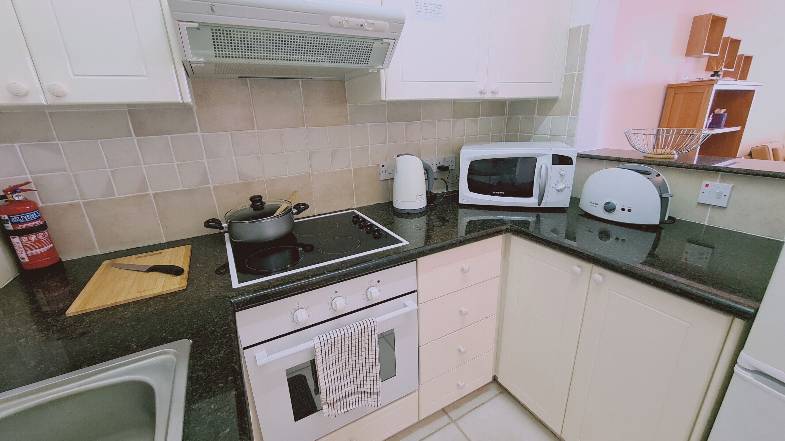 Une cuisine compacte équipée d’une cuisinière, d’un four à micro-ondes et d’un four traditionnel. On y trouve également un extincteur, une planche à découper et un évier.