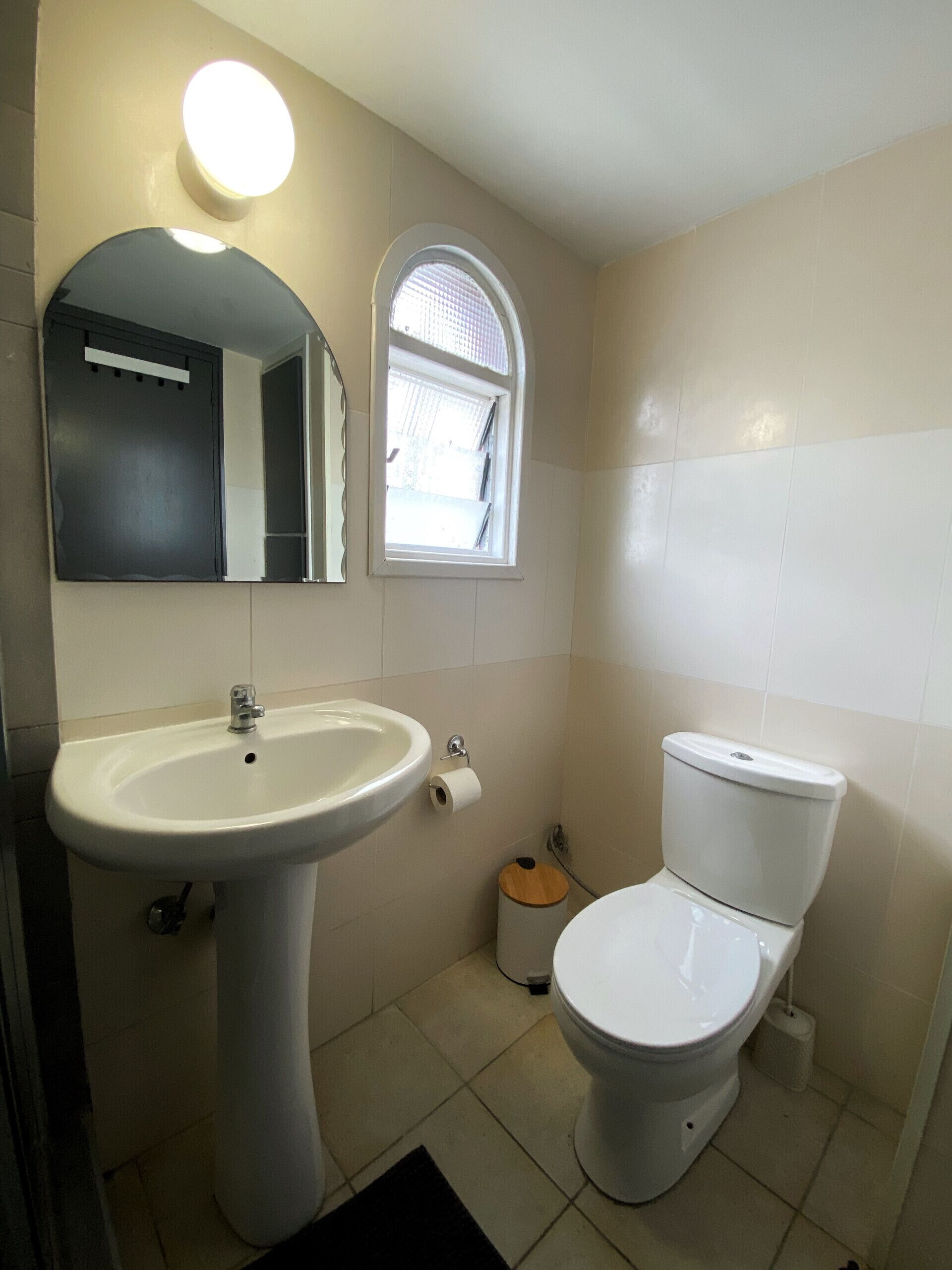 A bathroom with a pedestal sink, a toilet, a mirror, and a window.