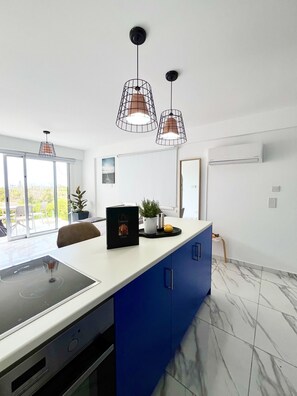 A modern kitchen with a central island, pendant lights, and a view to the outside.