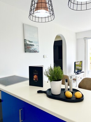 A kitchen with a white countertop, a potted plant, a book titled 'The Della Collection,' and a black tray with lemons. - STAY Elias Garden Apartment (Protaras)
