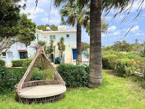 A house with a garden, a swing chair, and palm trees. - STAY Elias Garden Apartment (Protaras)