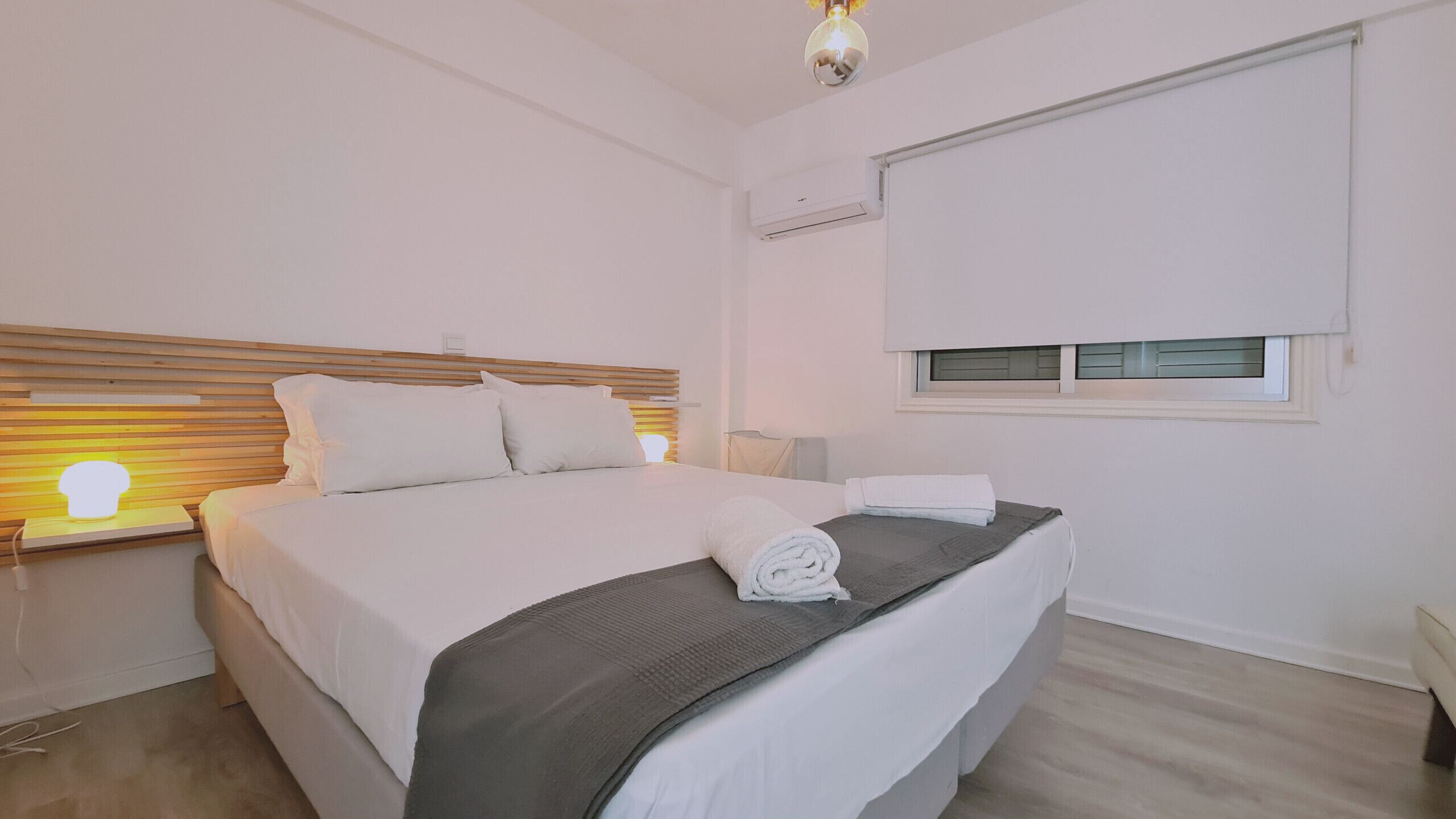 Een slaapkamer met een bed, bedlampje, raam en airconditioning.