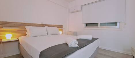 Een slaapkamer met een bed, bedlampje, raam en airconditioning.