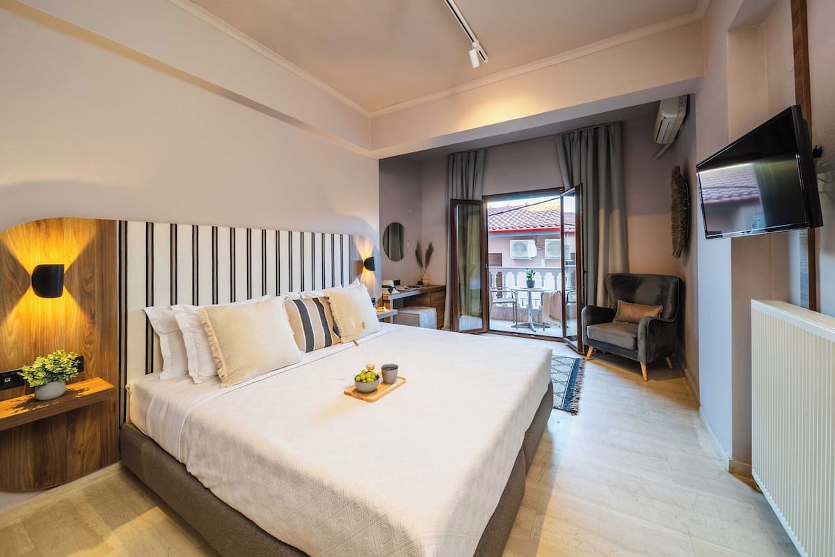 Une chambre d’hôtel moderne avec un grand lit, un téléviseur fixé au mur et un balcon avec vue.