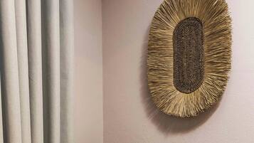 A dark grey armchair with wooden legs, a brown cushion, and a woven wall art piece above it.