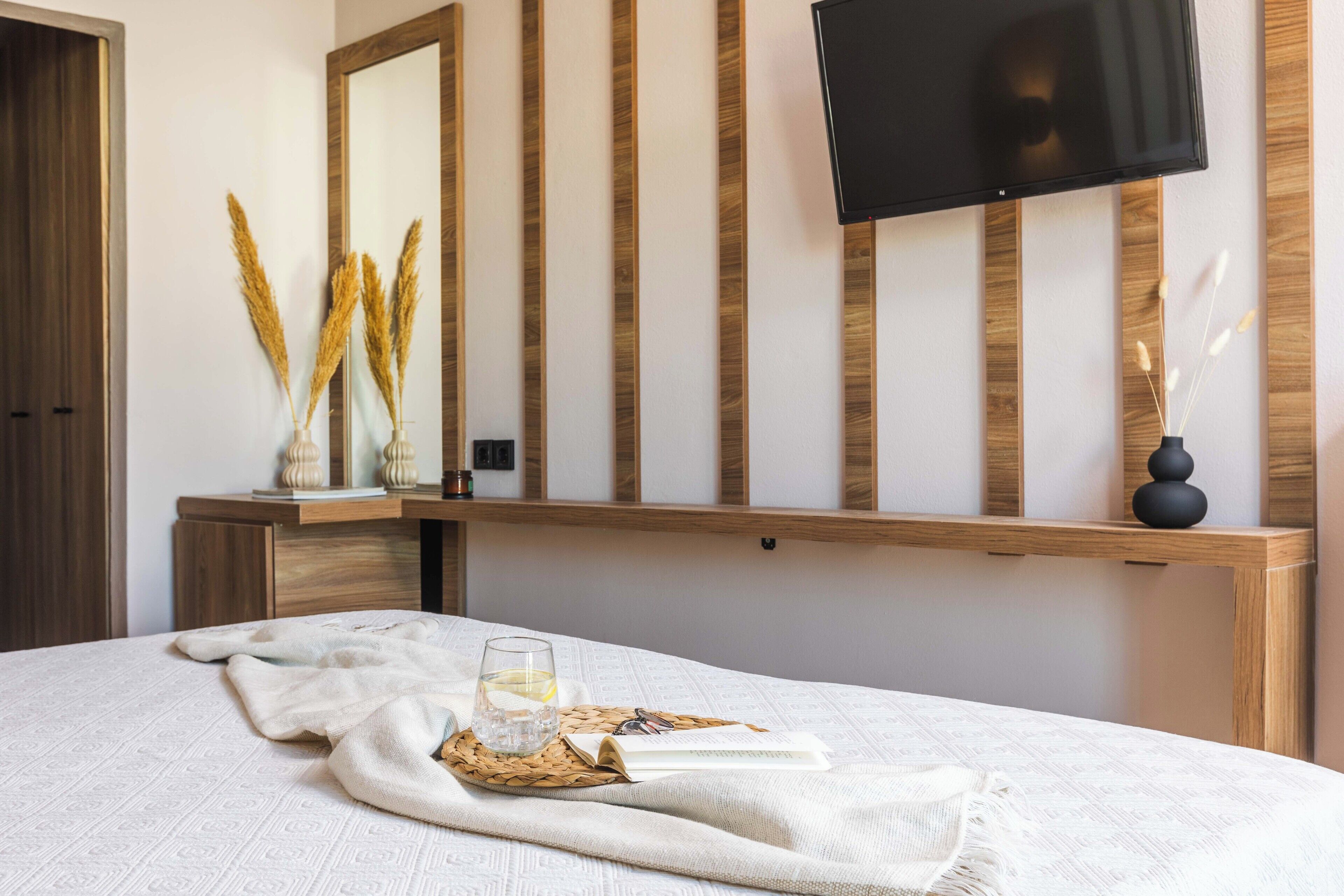 Un dormitorio ordenado con cama, mesita de noche y televisor montado.