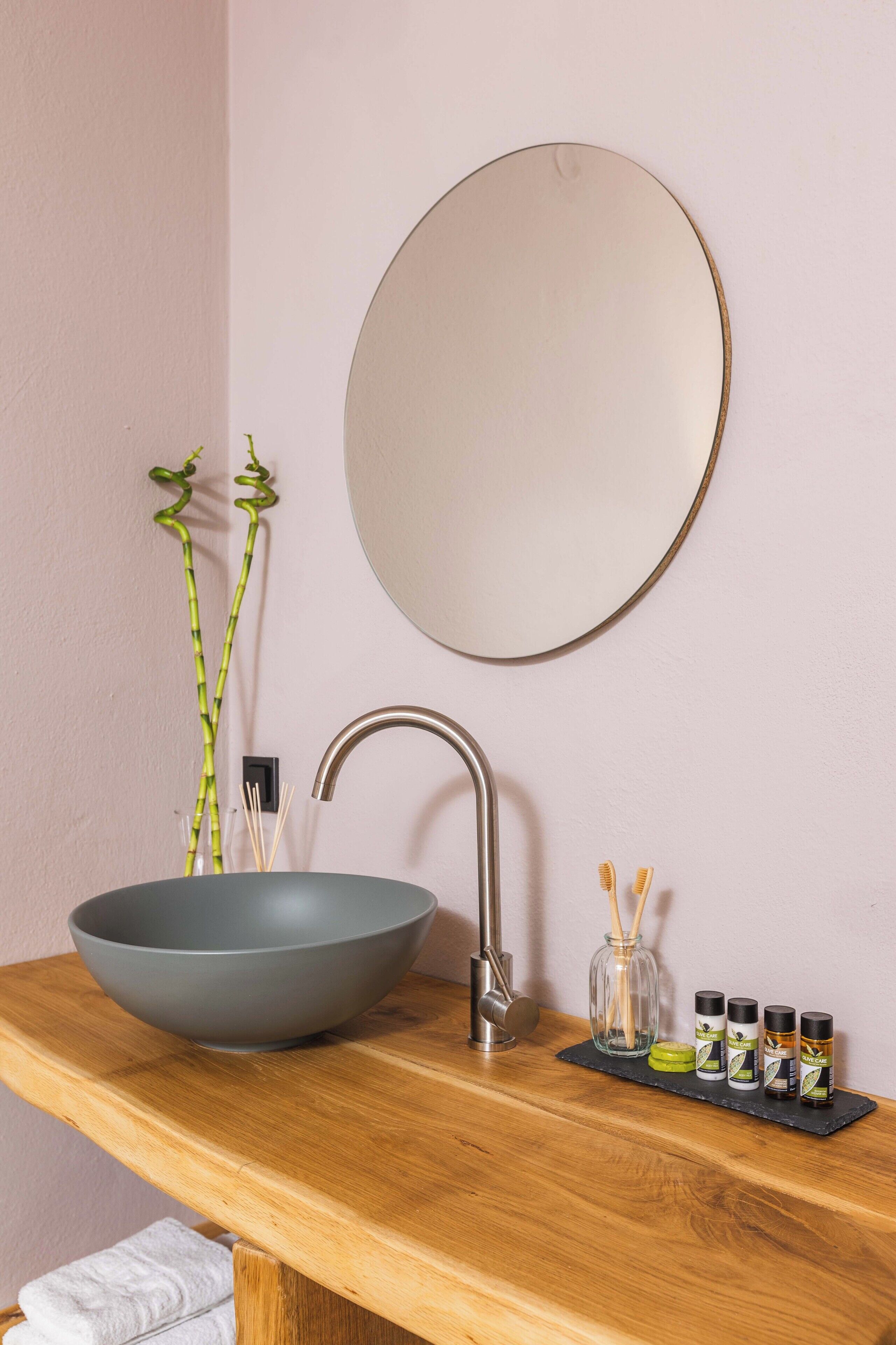 A bathroom with a wooden vanity, a large bowl sink, a mirror, and a small plant.