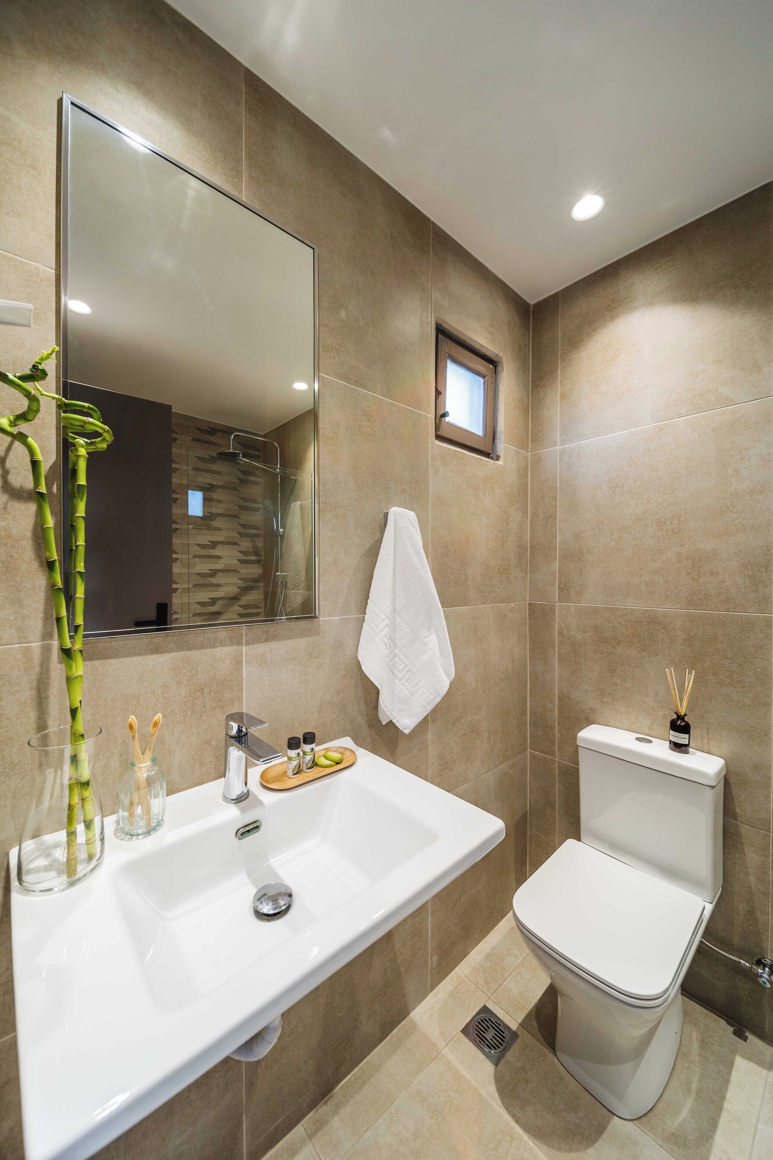 Un baño moderno con un espejo grande, un lavabo blanco, un inodoro y una ducha.