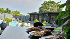 A dining table with various dishes, a pool, and a modern building in the background. - DE PORCH (Bolinao)