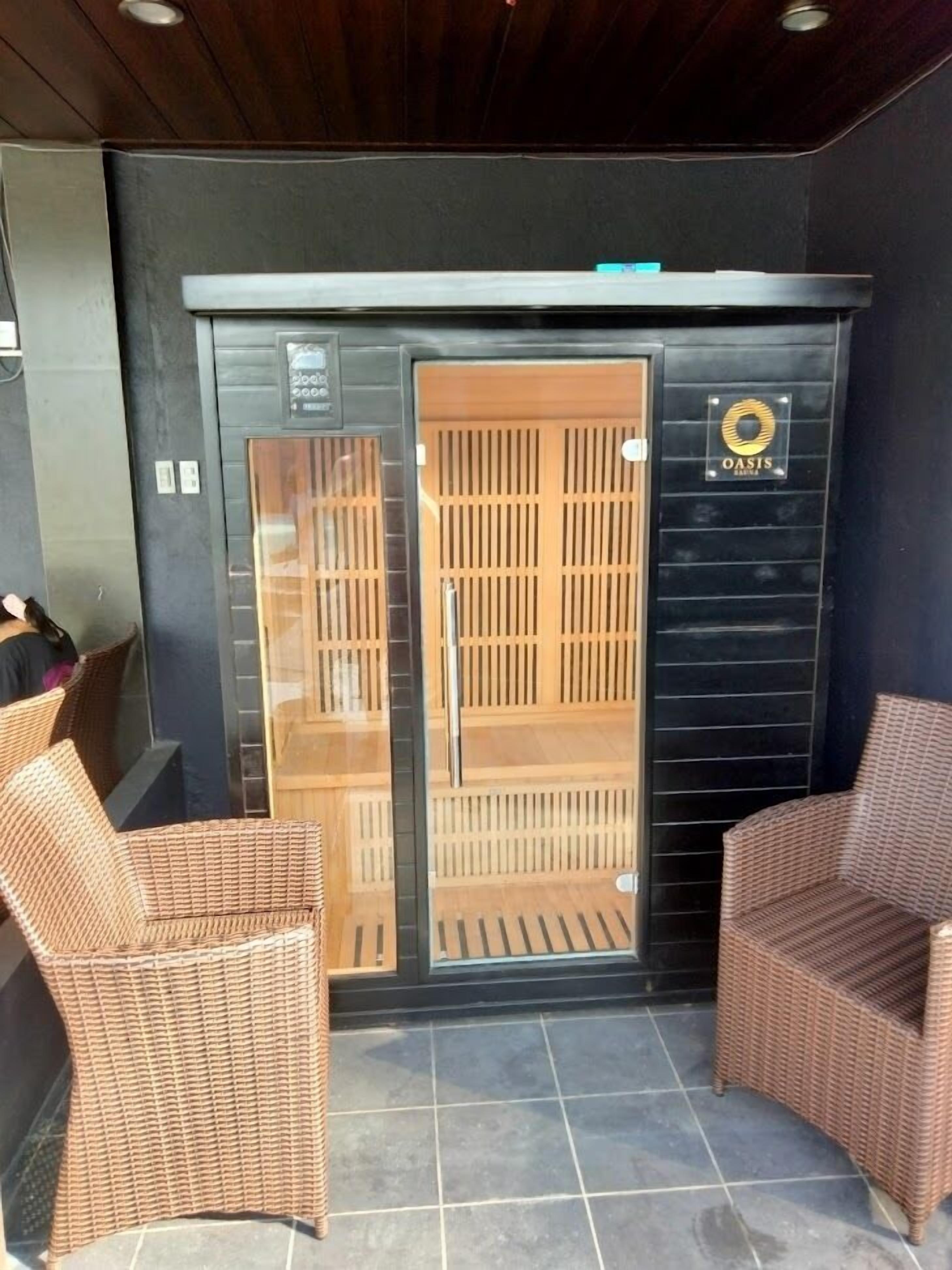 Une salle de spa dotée d’une porte en verre, de deux fauteuils en osier et d’un logo sur le mur.