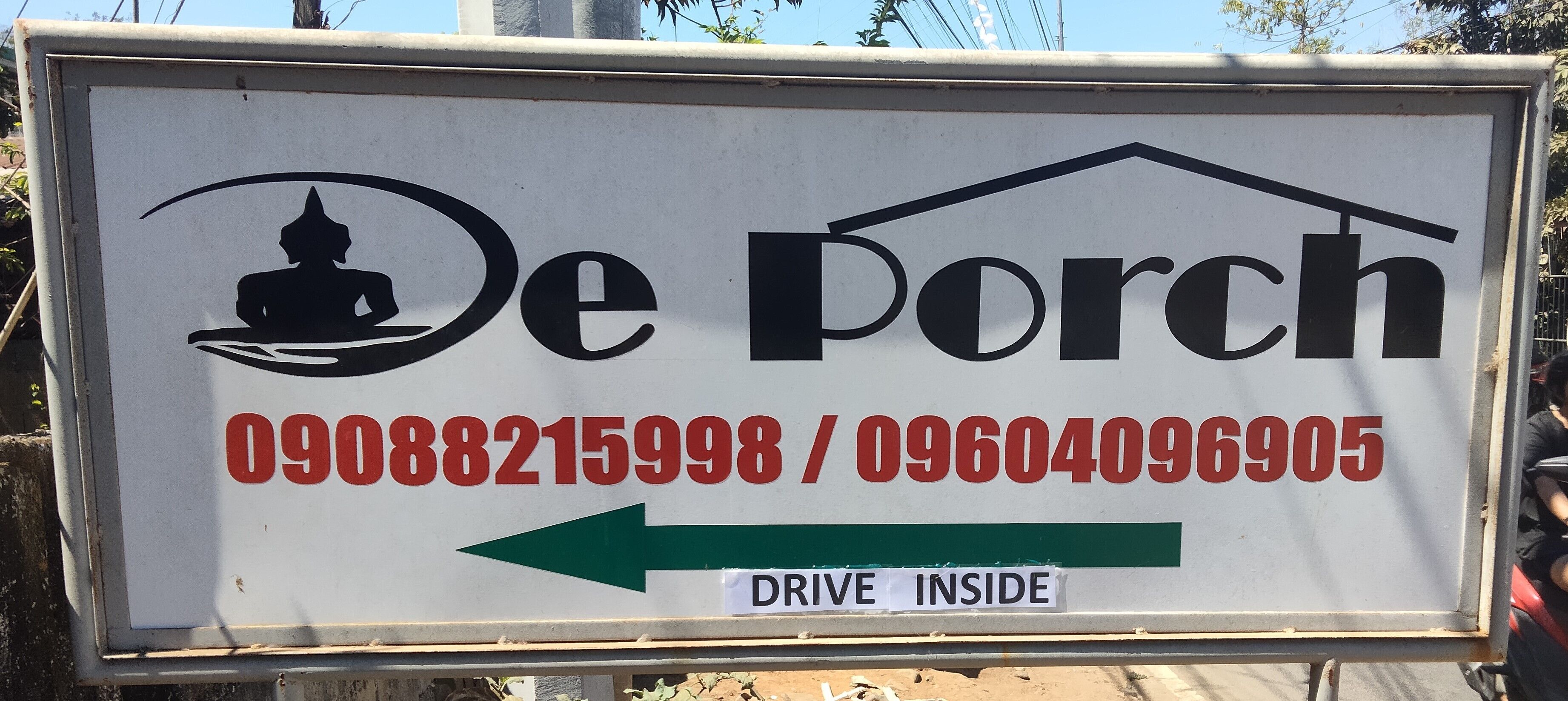 A sign for De Porch with contact numbers and a direction to drive inside.