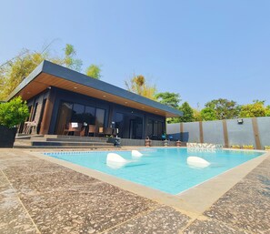 A modern poolside area with a rectangular pool, lounge chairs, and a building with large windows and a wooden roof. - DE PORCH (Bolinao)