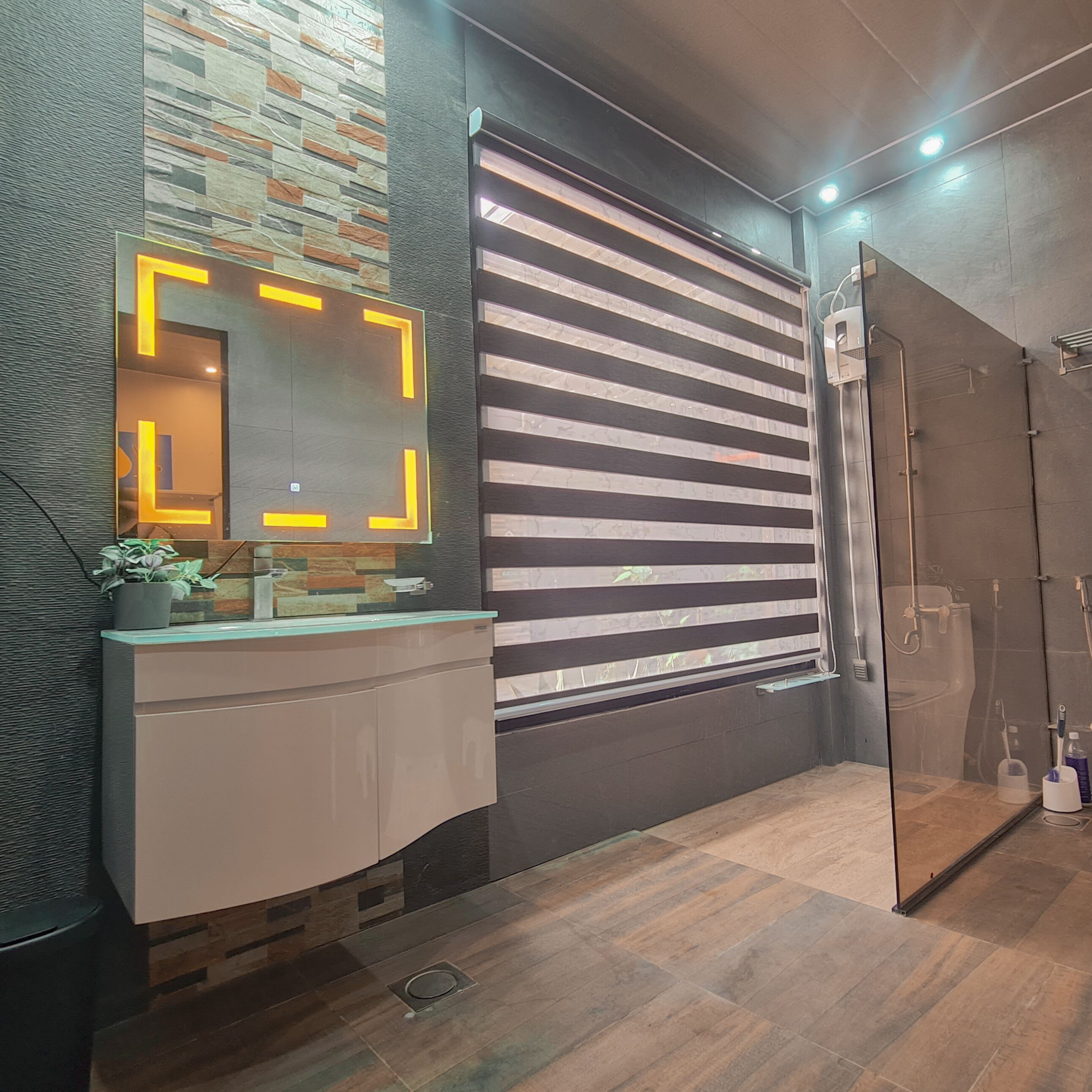 A modern bathroom with a large mirror, a shower, and a vanity with a potted plant.